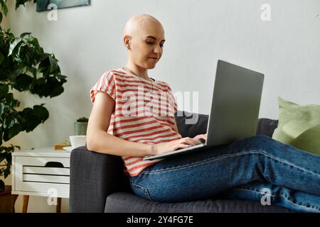 Eine junge kahlköpfige Frau sitzt bequem auf einer Couch, arbeitet an ihrem Laptop und zeigt ihren Fokus. Stockfoto