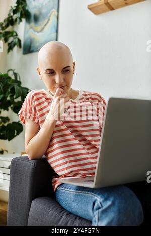 Eine Frau sitzt auf einem Stuhl, tief in Gedanken, während sie ihren Laptop durchsucht, lässig in Streifen gekleidet. Stockfoto