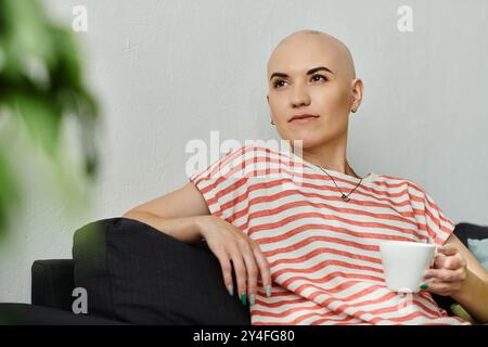 Eine junge kahlköpfige Frau sitzt bequem auf einer Couch, genießt ihren Kaffee und reflektiert friedlich. Stockfoto