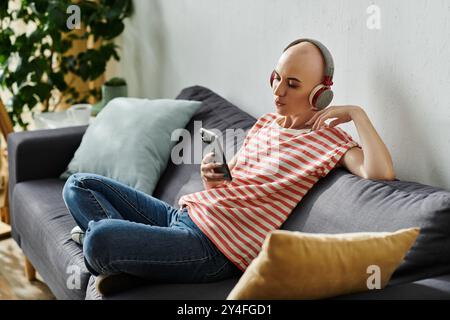 Eine schöne kahlköpfige Frau hört Musik, während sie sich auf einer bequemen Couch zu Hause entspannt. Stockfoto