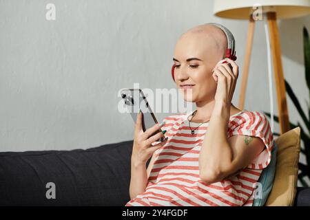 Eine junge kahlköpfige Frau lächelt, während sie in ihrem Haus Musik über Kopfhörer hört. Stockfoto