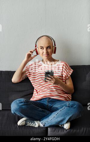 Eine fröhliche kahlköpfige Frau mit Alopezie entspannt sich auf einer Couch, eingetaucht in ihre Musik. Stockfoto