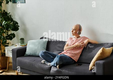 Eine kahlköpfige Frau mit Alopezie sitzt bequem auf einem Sofa und taucht in ihre Musik ein. Stockfoto