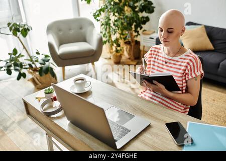 Eine junge kahlköpfige Frau schreibt in ihrem Notizbuch, während sie an einem gut beleuchteten Schreibtisch sitzt. Stockfoto