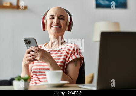 Eine junge kahlköpfige Frau lächelt, während sie Musik auf ihren Kopfhörern hört und ihr Smartphone hält. Stockfoto