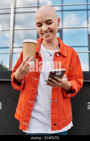 Eine junge kahlköpfige Frau lächelt, während sie eine Kaffeetasse hält und schreibt, was Glück ausstrahlt. Stockfoto