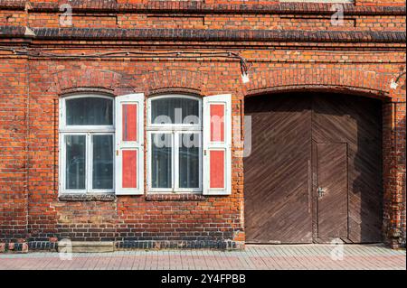 Backsteinbau mit roten Fensterläden und einer Holztür vor einem klaren Himmel. Stockfoto