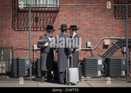 3 orthodoxe jüdische Männer mit Koffern warten auf einen Bus, nachdem sie Shabbat in Williamsburg, Brooklyn, verbracht haben. Stockfoto