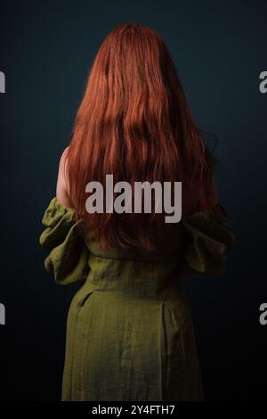 Rückansicht einer mysteriösen Frau mit langen roten Haaren, die ein Vintage-grünes Kleid trug, das ihr von der Schulter rutschte Stockfoto
