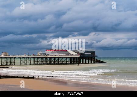 Blick vom Meer auf die RNLI Rettungsbootstaion und Pavilion Theatre am Pier unter einem dunklen bewölkten Himmel. Cromer, Norfolk, East Anglia, England, Vereinigtes Königreich, Großbritannien Stockfoto