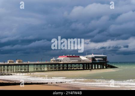 Blick vom Meer auf die RNLI Rettungsbootstaion und Pavilion Theatre am Pier unter einem dunklen bewölkten Himmel. Cromer, Norfolk, East Anglia, England, Vereinigtes Königreich, Großbritannien Stockfoto