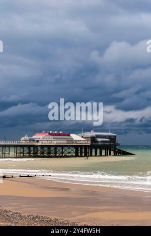 Blick vom Meer auf die RNLI Rettungsbootstaion und Pavilion Theatre am Pier unter einem dunklen bewölkten Himmel. Cromer, Norfolk, East Anglia, England, Vereinigtes Königreich, Großbritannien Stockfoto