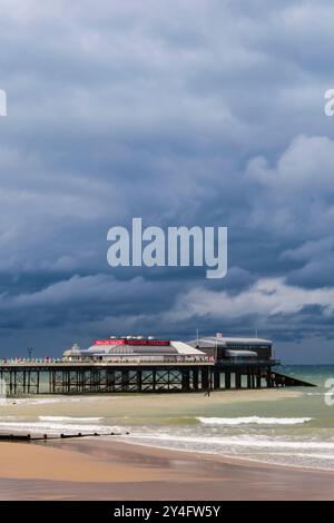 Blick vom Meer auf die RNLI Rettungsbootstaion und Pavilion Theatre am Pier unter einem dunklen bewölkten Himmel. Cromer, Norfolk, East Anglia, England, Vereinigtes Königreich, Großbritannien Stockfoto