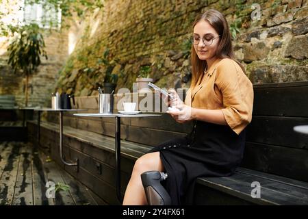 Eine junge Frau entspannt sich in einem gemütlichen Café, während sie mit ihrem Smartphone ihre Beinprothese vorstellt. Stockfoto