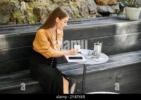 In einem ruhigen Café schreibt eine junge Frau mit einer Beinprothese in ihr Tagebuch, während sie Kaffee trinkt. Stockfoto