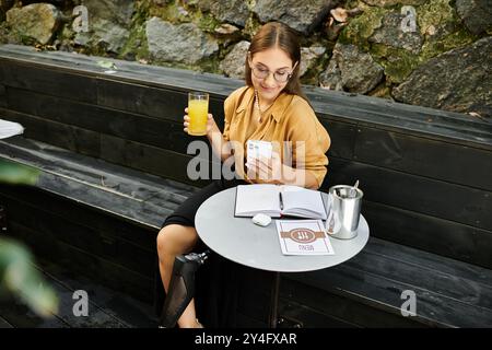 In einem gemütlichen Café lächelt eine junge Frau mit einer Beinprothese an ihrem Telefon, während sie einen erfrischenden Drink schlürft. Stockfoto