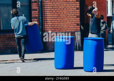 Ein junger Mann trägt ein großes blaues Fass, mehrere blaue Fässer im Hintergrund, Gehweg, von hinten fotografiert Stockfoto