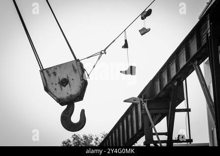 Detaillierte Aufnahme eines großen Kranhakens, hervorgehoben durch ein Paar alte Schuhe, die neben dem Kranhaken hängen, fineart-Foto Stockfoto