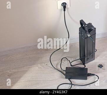 Laden der Fahrradbatterie über das Stromnetz im Haus. Steckdose im Zimmer mit eingeschaltetem Stecker. Umweltfreundlicher Transport. Stockfoto