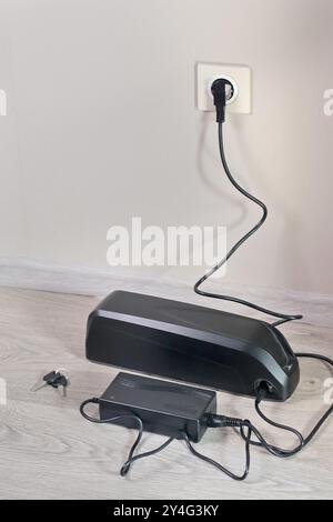 Laden der Fahrradbatterie über das Stromnetz im Haus. Steckdose im Zimmer mit eingeschaltetem Stecker. Umweltfreundlicher Transport. Stockfoto