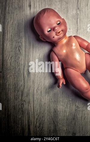 Eine gruselige Vintage-Puppe liegt auf einem grauen Holzboden und erinnert an Nostalgie und Einsamkeit in einer eindringlichen Atmosphäre Stockfoto