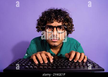 Nahaufnahme Foto von einem arabischen Mann, der Programmierer arbeitet, der auf pc-Bildschirm mit Tastatur schaute und eine Brille trug, die auf violettem Hintergrund isoliert war Stockfoto
