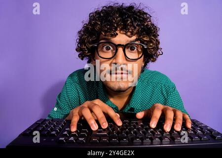 Nahaufnahme eines arabischen Guy begeisterte Programmierers, der auf dem pc-Bildschirm mit der Tastatur eine Brille auf violettem Hintergrund trug Stockfoto