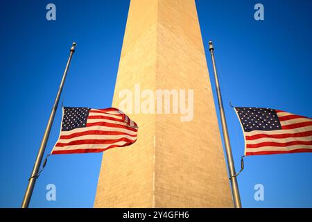 WASHINGTON DC, Vereinigte Staaten – die Flaggen um den Fuß des Washington Monuments fliegen mit Halbmast im warmen Glanz der Nachmittagssonne. Diese feierliche Ausstellung in der National Mall dient als visuelle Darstellung der nationalen Trauer oder Erinnerung, mit dem ikonischen Obelisken hoch im Hintergrund. Stockfoto