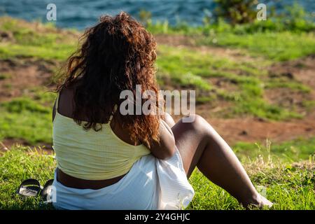 Frau entspannt sich im Gras während Sonnenuntergang. Eine junge Frau in übergroßer Größe Afroamerikanerin, die sich im Sommerpark im Freien entspannt und sich positiv auf den Körper einlässt. H Stockfoto