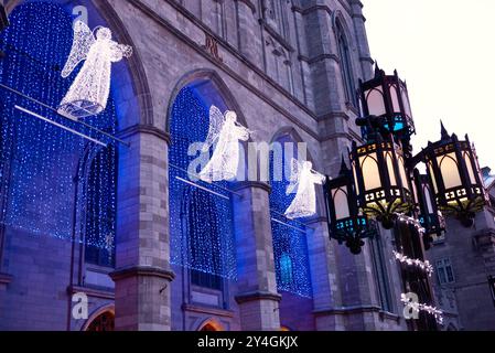 MONTREAL, Kanada – die Engelsleuchten beleuchten den Eingang der Basilika Notre-Dame in der Weihnachtszeit im Revival der Gotik. Die historische katholische Kirche, die 1829 fertiggestellt wurde, steht als Herzstück der Feierlichkeiten in Montreal im Stadtteil Old Montreal. Die dramatische Beleuchtung unterstreicht die architektonischen Details der Basilika und schafft eine festliche Atmosphäre für Winterbesucher. Stockfoto