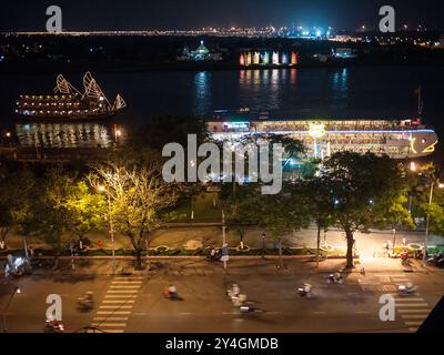 Saigon River Waterfront Night View Ho Chi Minh City Vietnam // HO CHI MINH CITY, Vietnam - erhöhter nächtlicher Blick auf den Saigon River, der die lebhafte Aktivität am Ufer mit beleuchteten Flussufern und belebtem Straßenverkehr entlang des Flussufers zeigt. Die Szene fängt die dynamische Energie von Vietnams größter Stadt ein, in der traditioneller Fluss-Handel auf moderne Stadtentwicklung trifft. Stockfoto