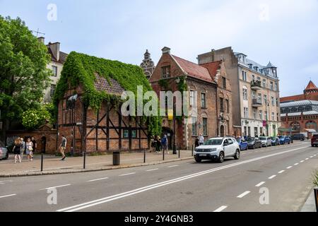 Blick auf die Straße in Danzig, Polen, mit einem historischen, mit Efeu bedeckten Haus mit traditioneller Backstein- und Holzarchitektur entlang einer befahrenen Straße. Stockfoto