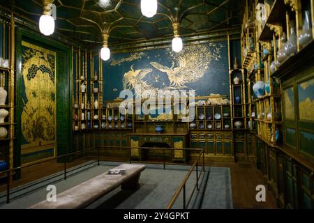 WASHINGTON, D.C. — Ein Wandbild mit zwei kämpfenden Pfauen ziert die Südwand von James McNeill Whistlers berühmtem Pfauraum im National Museum of Asian Art Dieses Wandgemälde mit dem Titel „Art and Money; Or, The Story of the Room“ wurde 1876–1877 geschaffen und stellt Whistlers künstlerische Vergeltung gegen seinen Mäzen Frederick Richards Leyland nach deren bitterem Finanzstreit dar. Der Pfau auf der rechten Seite, der Leyland repräsentiert, weist silberne Kehlfedern auf, die auf die markanten weißen Rüschenhemden des Schifffahrtsmagnaten verweisen, während der linke Pfau, der Whistler repräsentiert, ein Silber trägt Stockfoto