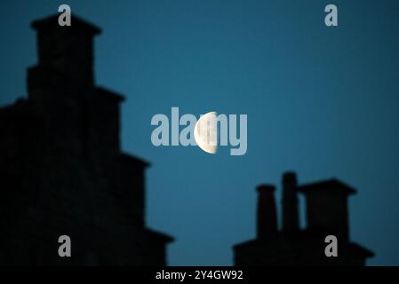 Der Mond in seinem dritten Viertel liegt am Himmel vor der Dämmerung hinter Schornsteinen einiger der historischen Gebäude auf einer Straße, die vom Markt im HIS abstrahlt Stockfoto