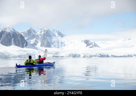 Petermann Island Kajakfahren Penola Strait Antarktische Halbinsel Sommer mit Menschen / PETERMANN ISLAND, Antarktis — zwei Kajakfahrer paddeln aktiv durch die Penola Strait vor Petermann Island, mit schneegefüllten Couloirs und Gletschern der Graham Coast, die steil hinter ihnen aufsteigen. Die Insel, die 1873–74 von der deutschen Expedition Eduard Dallmanns nach dem Gothaer Geographen August Petermann benannt wurde, liegt bei 65°10 in der Nähe des südlichen Eingangs des Lemaire-Kanals und ist heute einer der meistbesuchten touristischen Landeplätze der Antarktischen Halbinsel Stockfoto