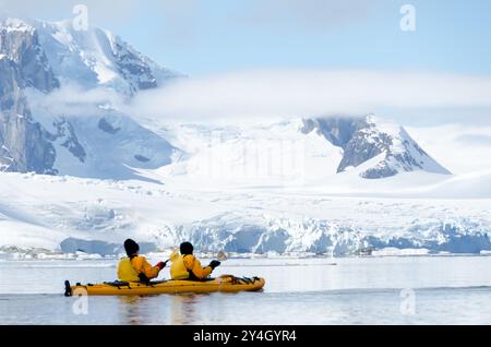 Petermann Island Kajak Antarctic Peninsula Sommer / PETERMANN ISLAND, Antarktis — zwei Expeditionskajaker in einem gelben Tandem-Meer Kajak paddeln im glasklaren Wasser von Port Circumcision, der geschützten Bucht an der Südostküste von Petermann Island, wo Jean-Baptiste Charcot sein Schiff Pourquoi-Pas überwinterte? Im Jahr 1909. Charcot benannte die Bucht, weil er sie am 1. Januar, dem katholischen fest der Beschneidung, gesehen hatte; der Name ist noch mehr als ein Jahrhundert später offiziell. Stockfoto