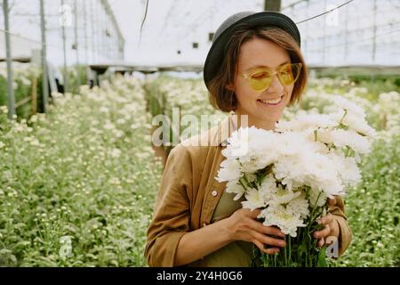 Lächelnde Frau, die weiße Blumen im Gewächshaus hält Stockfoto
