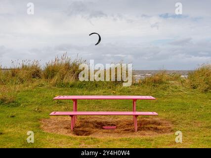 Eine pinkfarbene Picknickbank vor Kitesurfen und Kiteboarden am Nordstrand des Barassie Beach, in der Nähe von Troon in Schottland während eines windigen Summs Stockfoto