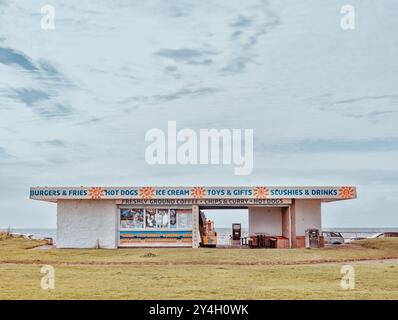 Ein aus Beton und Backstein bestehendes Diner-Gebäude, in dem während eines windigen Sommers im Jahr 2024 Fastfood und Strandspielzeug am Meer in Ayr in Schottland verkauft werden Stockfoto