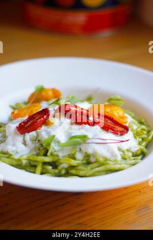 Nahaufnahme italienischer Trofia-Pasta mit Pesto, Burrata und Kirschtomaten, serviert auf einem weißen Teller. Italienische (ligurische) Küche, selektiver Fokus Stockfoto