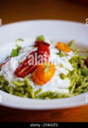 Nahaufnahme italienischer Trofia-Pasta mit Pesto, Burrata und Kirschtomaten, serviert auf einem weißen Teller. Italienische (ligurische) Küche, selektiver Fokus Stockfoto