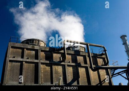 Dampf steigt aus Kühltürmen einer Chemiefabrik in Huelva, Andalusien, und zeigt die industrielle Aktivität unter einem klaren blauen Himmel. Stockfoto