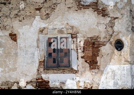 Architektonisches Detail einer grungy baufälligen Fassade eines verlassenen, mit Putz und Ziegelsteinen versehenen, verkleideten Gebäudes Stockfoto