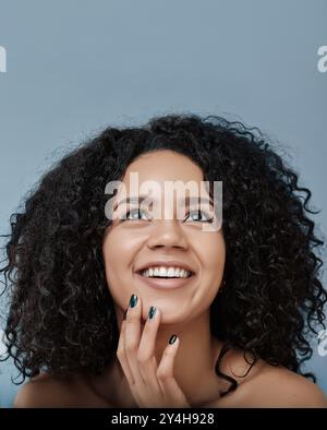 Nahaufnahme einer glücklichen jungen Frau, die aufblickt. Porträt einer Frau mit lockigem Haar, die lächelnd und aufblickend ist. Stockfoto