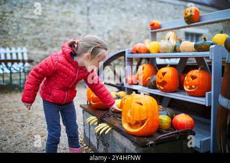 Entzückendes Mädchen im Vorschulalter, das Jack-o-Laterne Kürbis auf der Farm auswählt. Glückliches Kind, das Halloween feiert Stockfoto