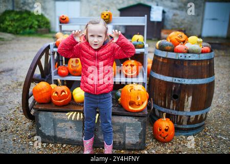 Entzückendes Mädchen im Vorschulalter, das Jack-o-Laterne Kürbis auf der Farm auswählt. Glückliches Kind, das Halloween feiert Stockfoto