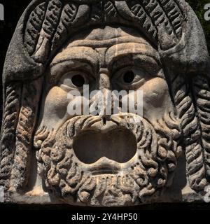 Nahaufnahme des überkreuzten Gesichts der römischen Theatermaske, das heute im römischen Theater in Ostia Antica, Italien, ausgestellt wurde und einst Teil der architektonischen Dekoration des Theaters war. Stockfoto