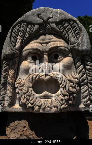 Das Gesicht der römischen Theatermaske mit überkreuzten Augen, das heute im römischen Theater in Ostia Antica, Italien, ausgestellt wurde und einst Teil der architektonischen Dekoration des Theaters war. Stockfoto