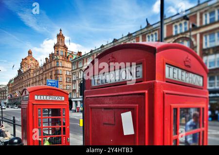 An der Brompton Road in der Nähe von Harrods stehen zwei berühmte rote Telefonzellen, die von einem hellblauen Himmel und dem geschäftigen Stadtleben umgeben sind. Stockfoto