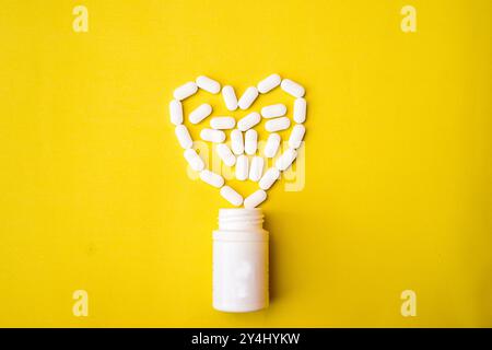 Das Herz aus Tabletten und Pillen auf gelbem Hintergrund. Verschiedene pharmazeutische Arzneimittel Pillen, Tabletten und Kapseln und Flasche auf gelbem Hintergrund Stockfoto